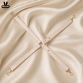 Adjustable blush pink four-point restraint connector strap system with gold-tone clips and central attachment ring.
